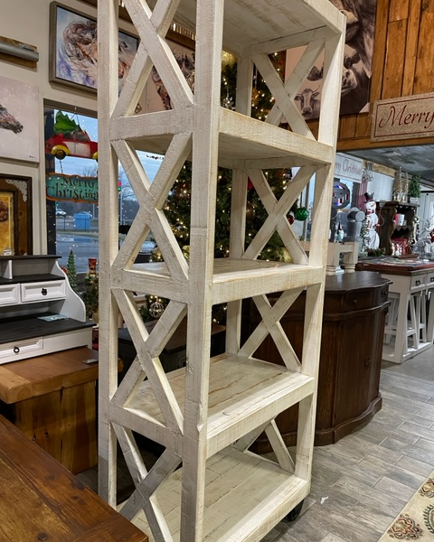 White wooden cross-braced shelf unit in a rustic interior, with framed art and decor in the background