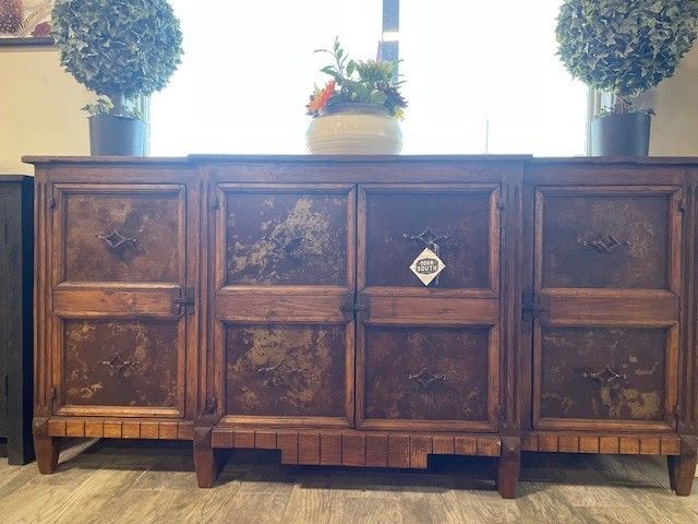 Wooden sideboard with paneled doors, flanked by two topiary plants and a small plant centerpiece.