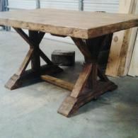 Rustic wooden table with thick plank top and X-shaped supports in a workshop setting