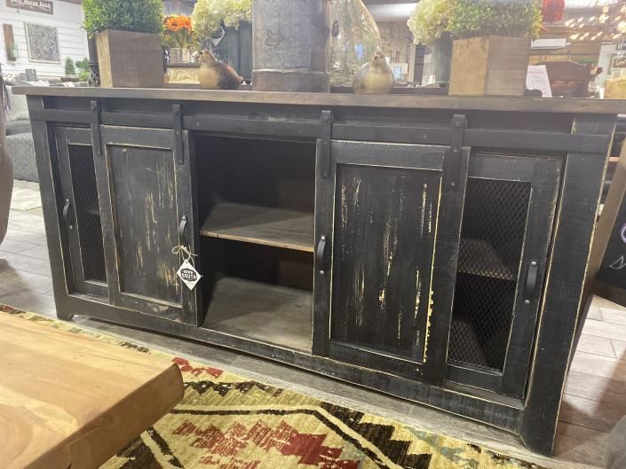 Black distressed wood TV console with open shelves and cabinet doors in a rustic living room