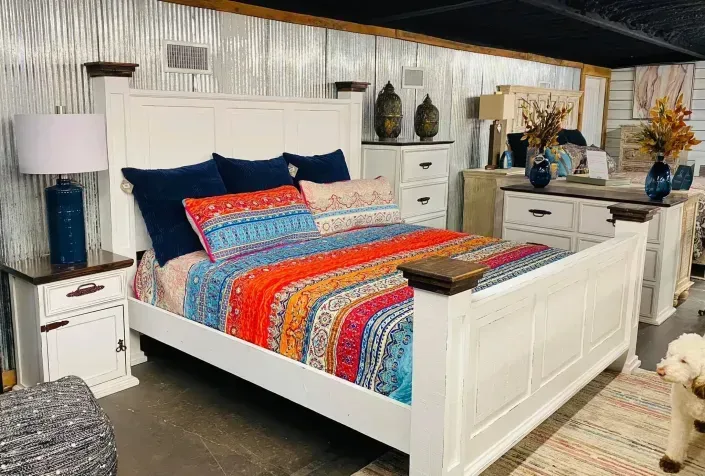 Colorful bed in a bright bedroom with white furniture, blue pillows, and patterned bedding