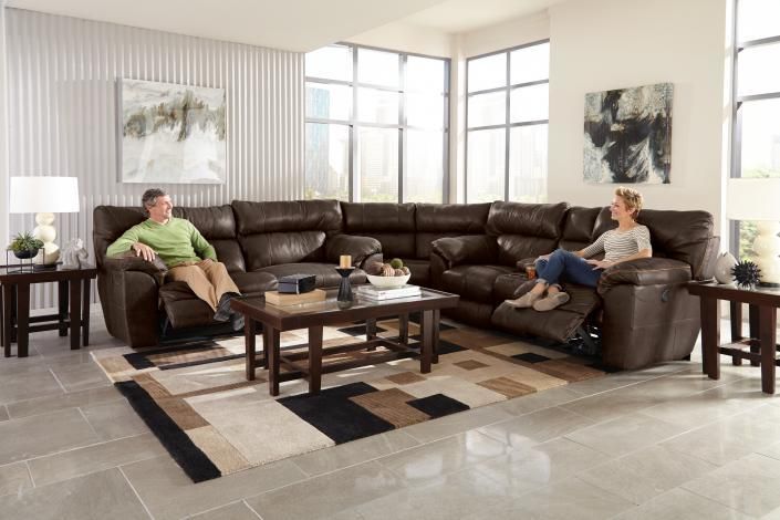 Living room with a brown sectional sofa, two people seated, coffee table, and large windows