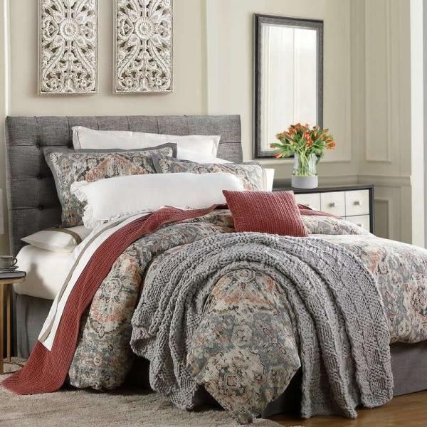 Cozy bedroom with a gray upholstered bed, patterned bedding, wall decor, and a vase of flowers on a side table