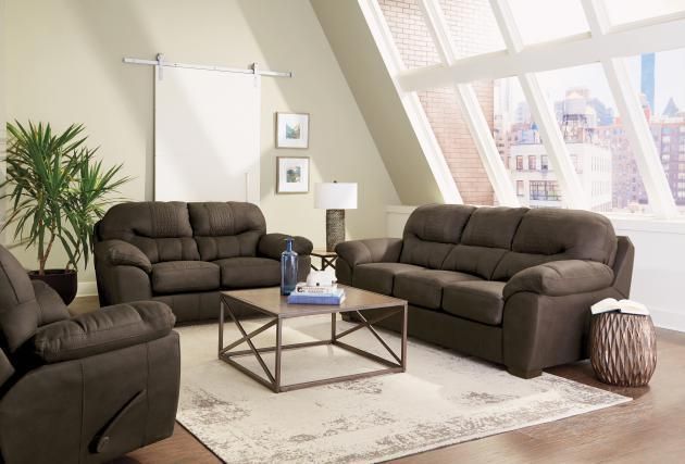Bright living room with dark sofas, coffee table, rug, plant, and large slanted windows