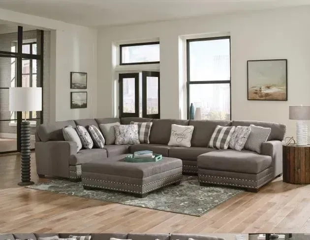 Modern living room with a gray sectional sofa, patterned ottoman, and large windows on hardwood floors