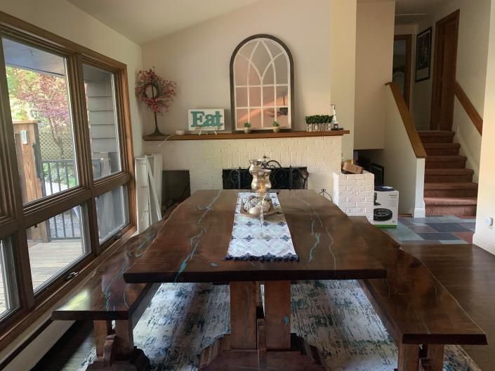 Dining room with wooden table, benches, fireplace mantel, and staircase in a bright home interior