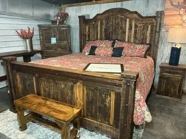 Rustic wooden bed with pink bedding in a cozy bedroom, with a bench at the foot and lamp on the side table