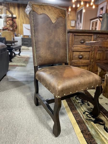 Brown leather upholstered dining chair with nailhead trim in a rustic furniture showroom