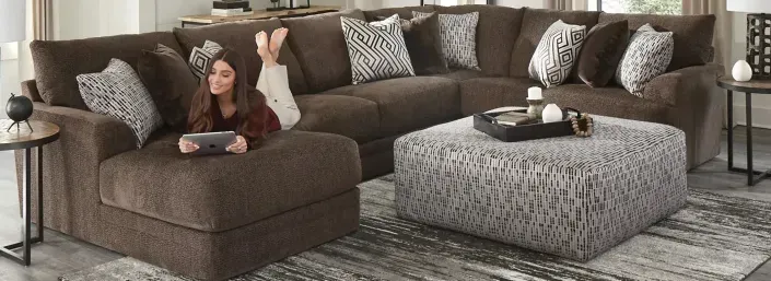 Living room with a brown sectional sofa, patterned pillows, and a large gray ottoman coffee table