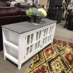 White farmhouse-style coffee table with gray top and decorative flowers in a living room showroom