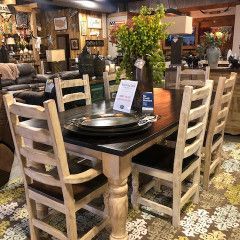 Rustic dining room display with a dark wood table, ladder-back chairs, dishes, and floral centerpieces