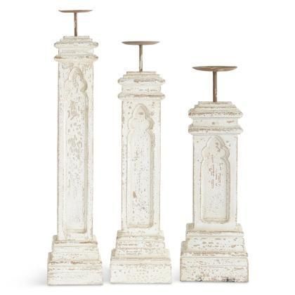 Three white weathered pedestal stands of varying heights with metal tops on a plain background