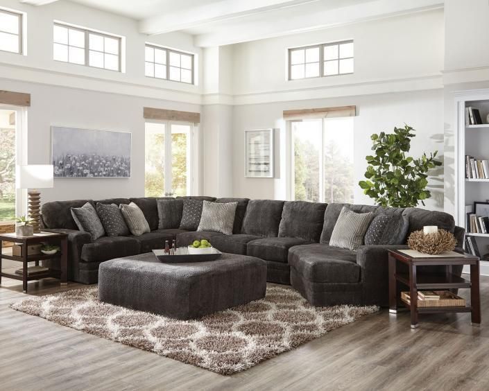 Bright living room with a dark gray sectional, matching ottoman, patterned rug, and large windows