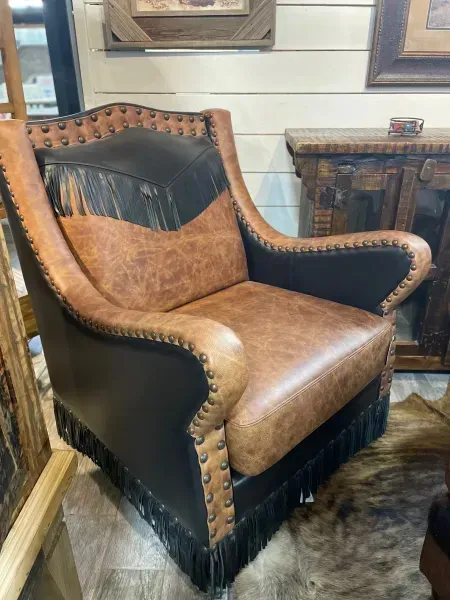 Brown leather armchair with black sides and fringe trim in a rustic room