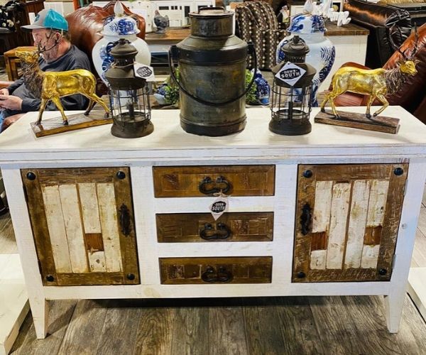 Rustic white dresser with antique lanterns and brass figurines displayed on top in a vintage shop