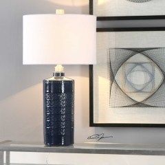 Blue table lamp with white shade beside framed abstract artwork on a shelf