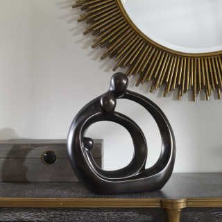 Abstract black metal sculpture on a shelf beneath a gold sunburst mirror on a gray wall