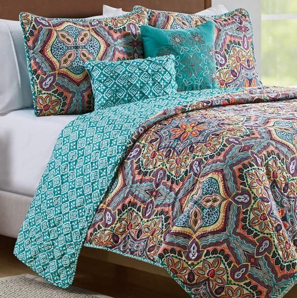 Colorful patterned bedding set with teal accent pillow and quilt on a white bed