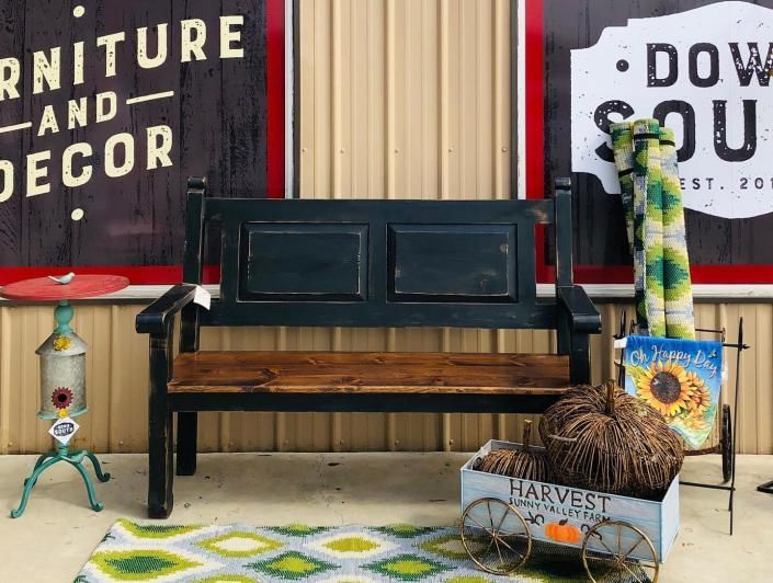 Black bench with wooden seat on patterned rug beside rustic outdoor decor and signs