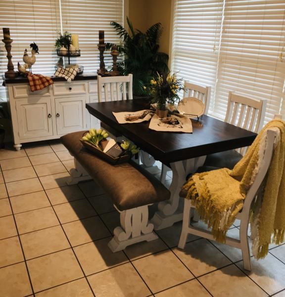 Bright dining nook with dark table, white chairs, bench, sideboard, plants, and beige tiled floor by windows