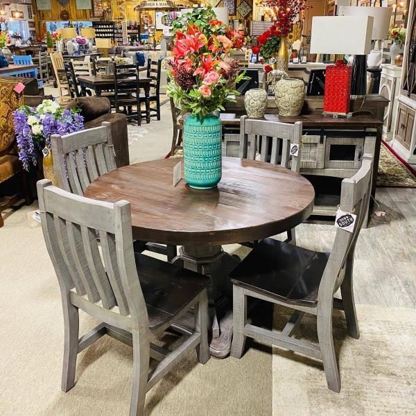 Round wooden table with four chairs and a vase of colorful flowers in a home decor store