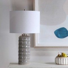 Textured table lamp with white shade beside abstract wall art and a small bowl of fruit