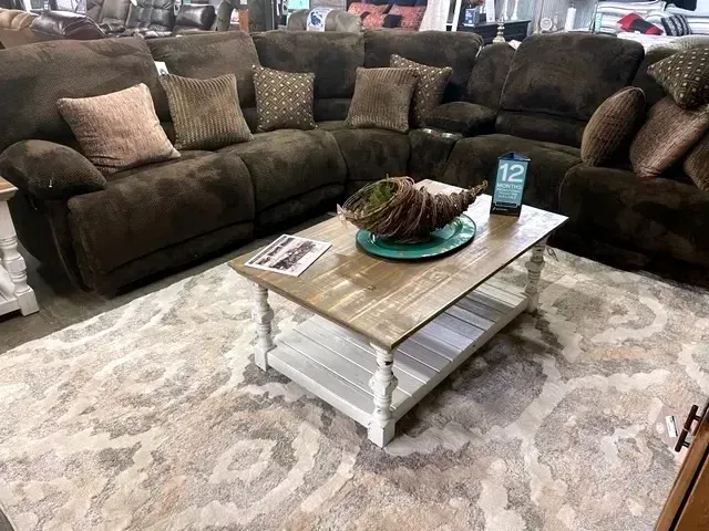 Brown sectional sofa around a rustic coffee table on a light patterned rug in a living room