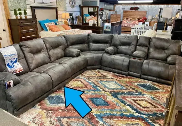 Gray sectional sofa with patterned rug in a furniture showroom, arrow pointing to the seat area
