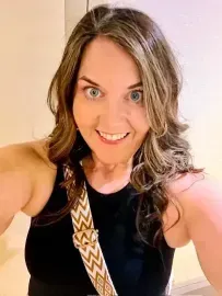 Smiling person in a black top with a patterned strap, taking a selfie indoors.