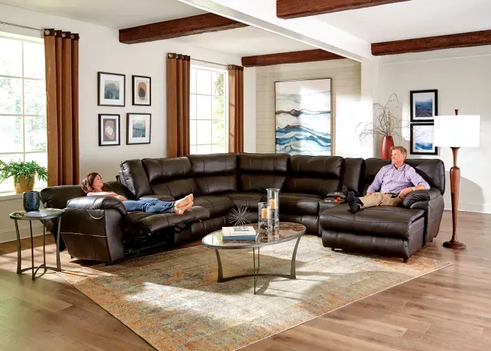 Modern living room with a black sectional, coffee table, and two people relaxing by large windows