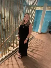 Woman in a black dress standing by a bamboo-style wall in a modern indoor hallway