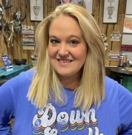 Smiling woman in a blue “Down” shirt standing indoors with rustic wooden decor behind her