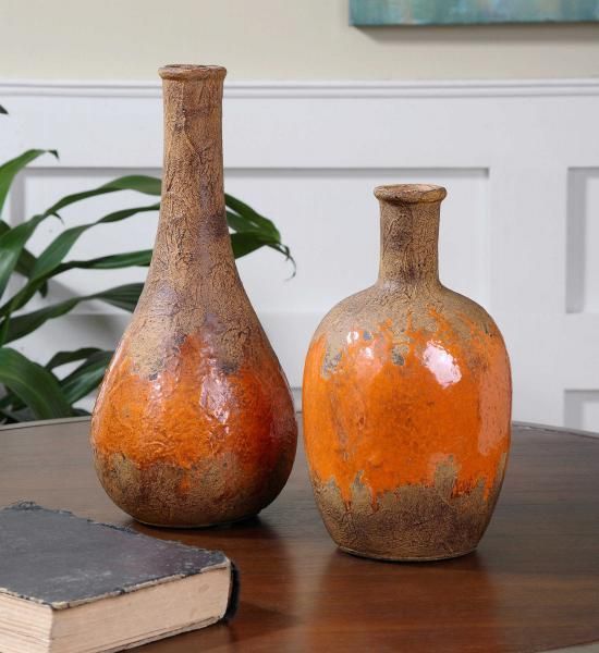 Two orange and brown ceramic vases on a wooden table with a book in the foreground