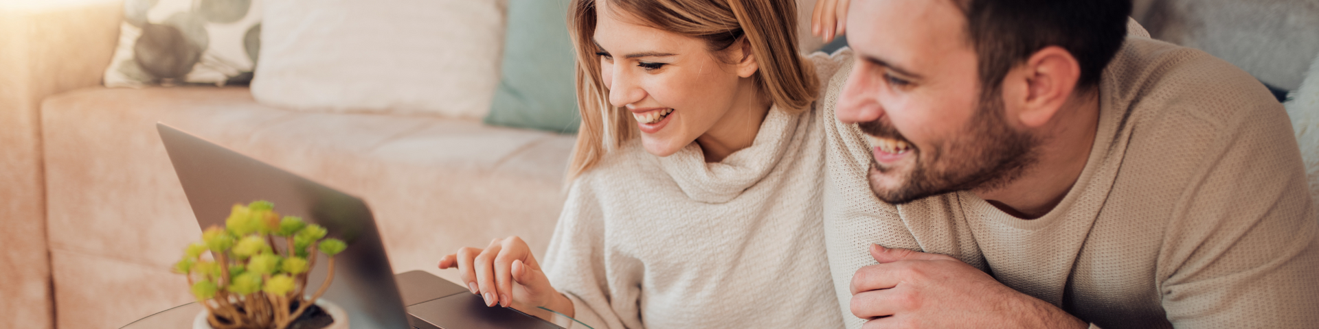 Two people smiling and looking at a laptop in a cozy living room while taking notes