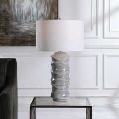White table lamp with a sculpted gray base on a glass side table in a paneled room