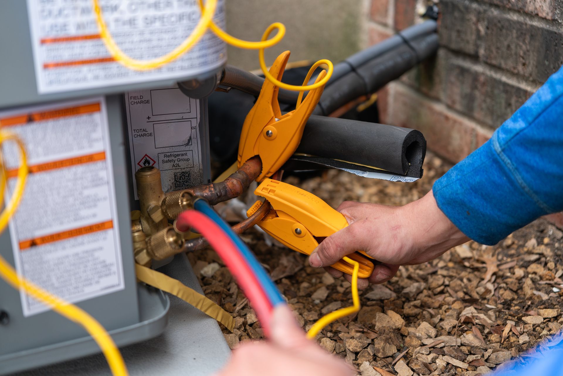HVAC technician connecting gauges to copper refrigerant lines on an outdoor air conditioner unit.