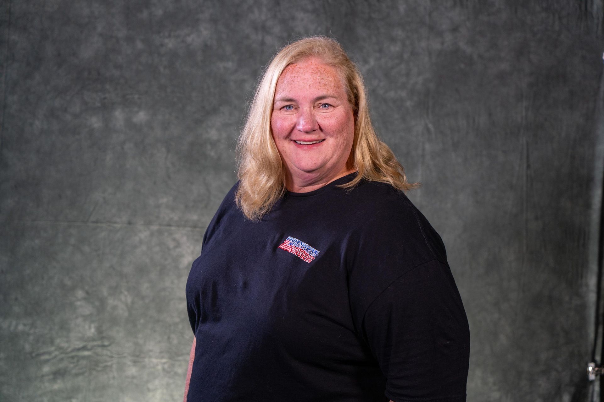Woman with blonde hair, wearing a black shirt, smiling against a gray backdrop.