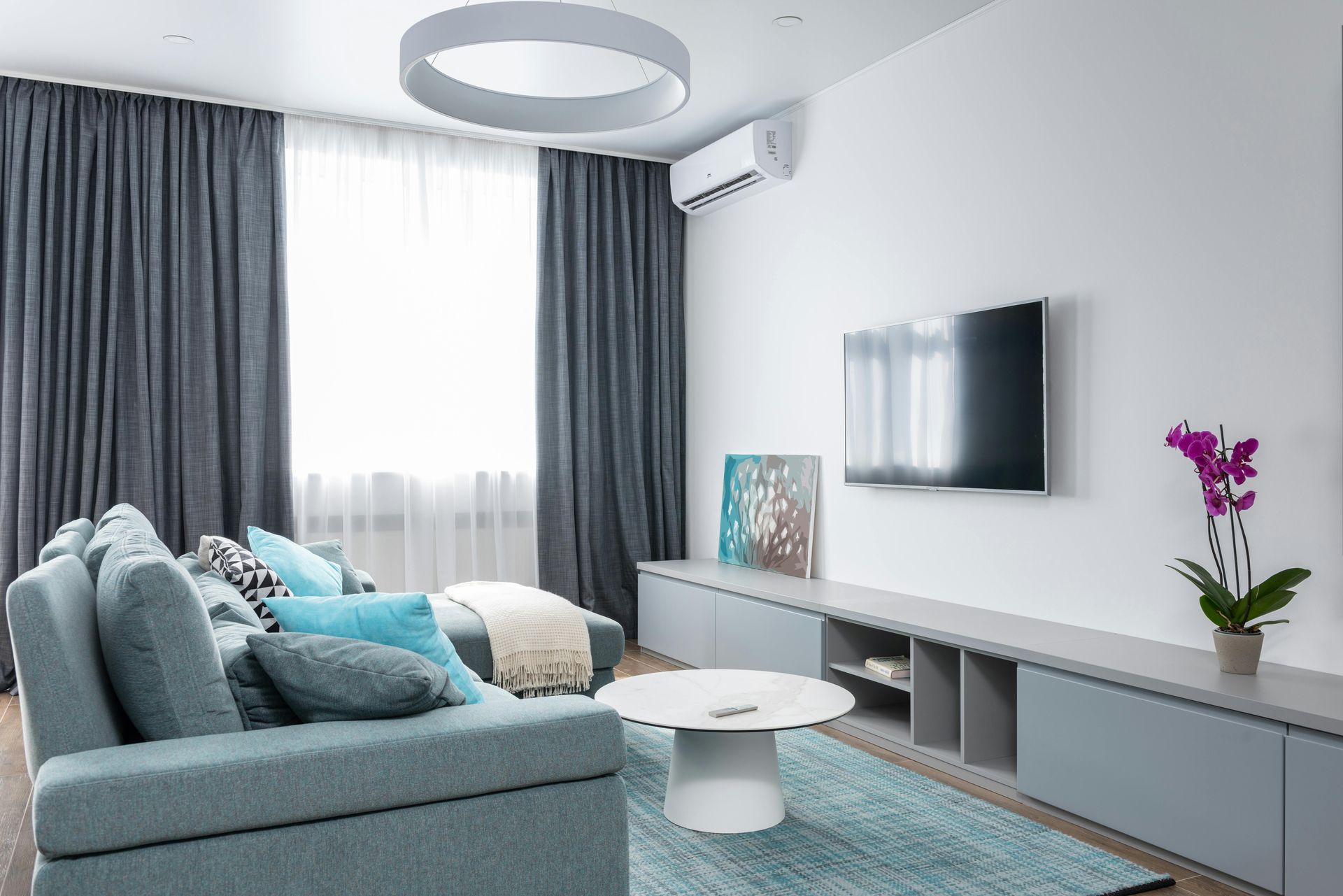 Modern living room with a blue sofa, gray curtains, and a mounted TV.