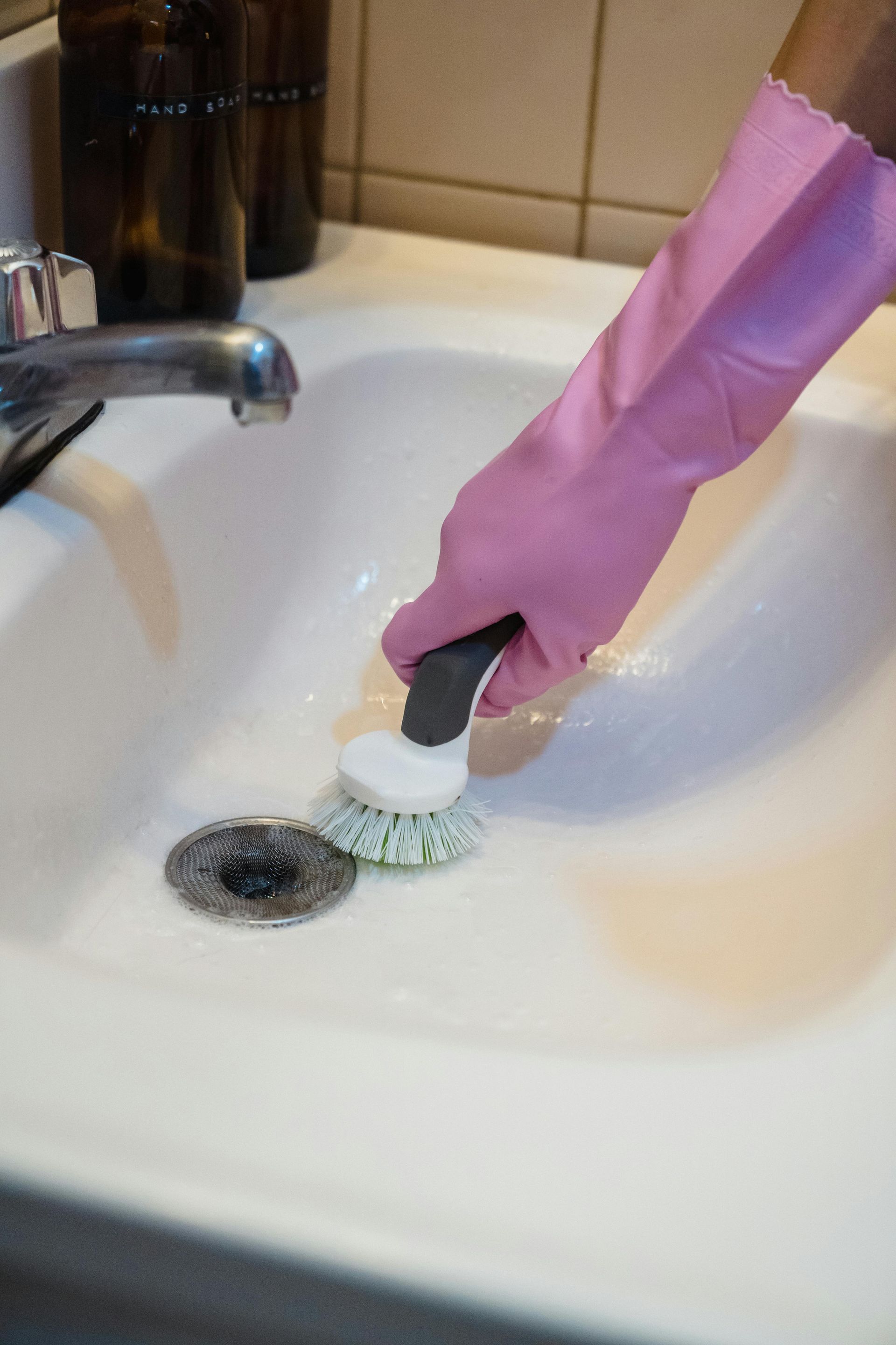Person in pink gloves scrubs a white sink with a brush.