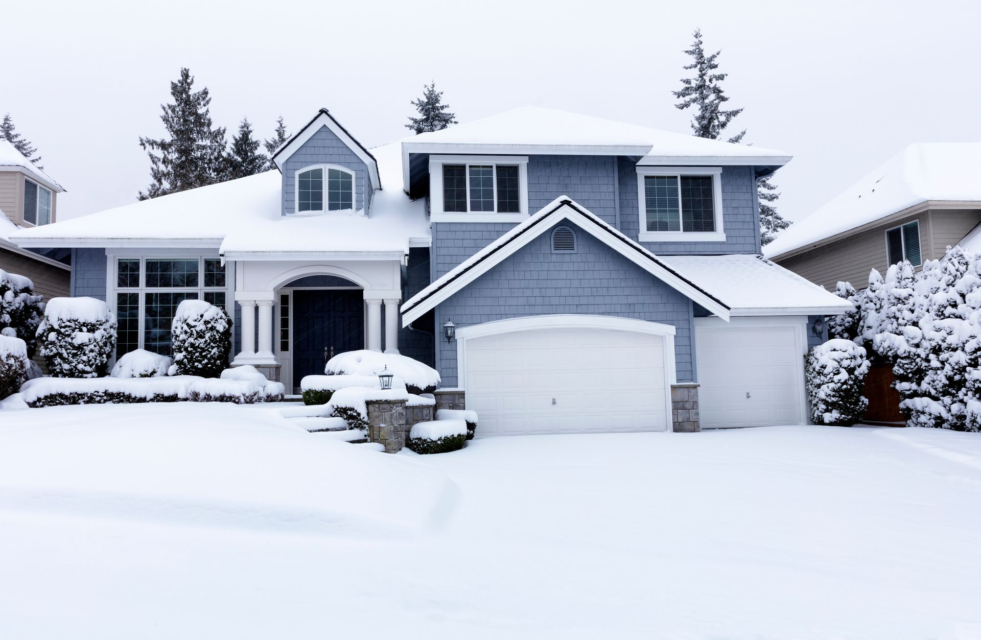 Snow-covered suburban house with garage and front yard after a heavy snowfall