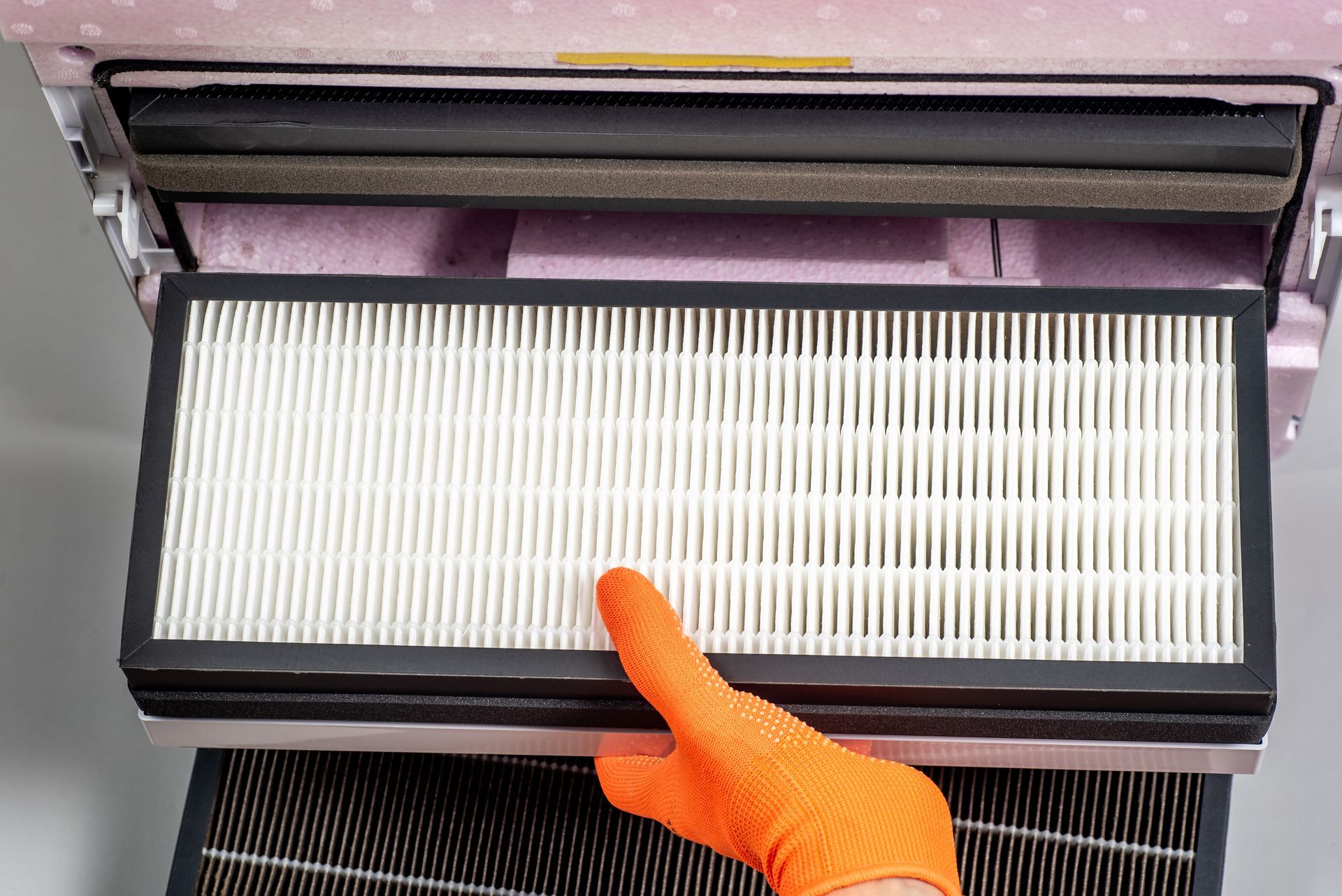 Hand in orange glove holding air filter from a pink polka-dotted air purifier.