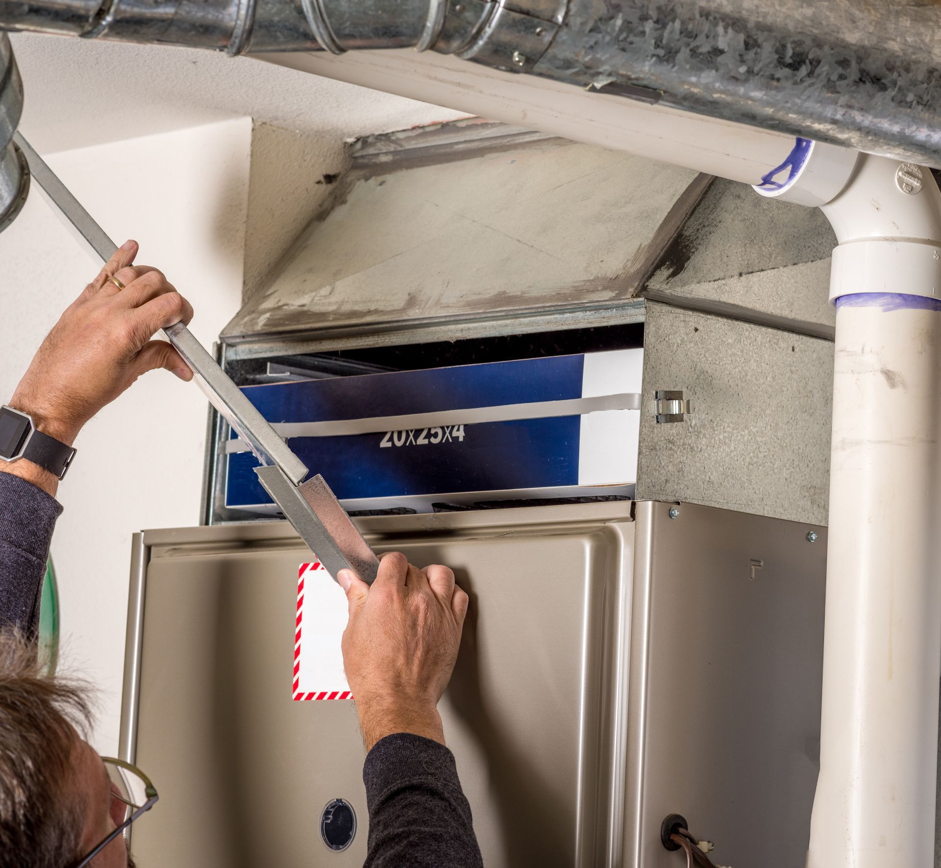 Person changing a furnace filter. Hands hold a metal tool to slide filter in a unit.