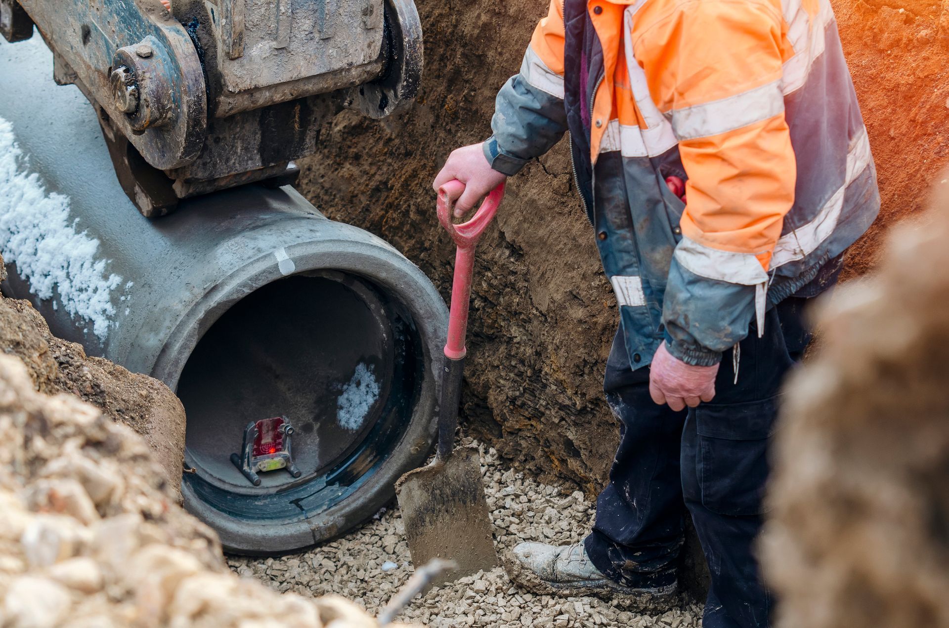 A man is digging a hole in the ground next to a pipe.