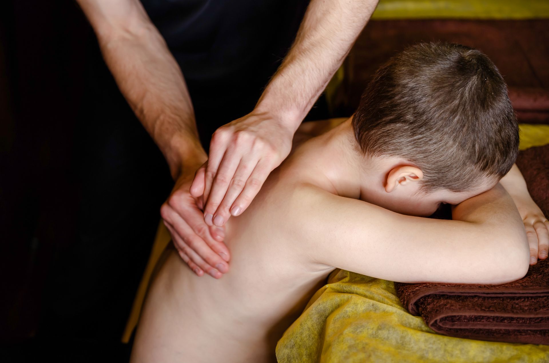 Massage therapist rubbing a child’s back on a towel-covered table
