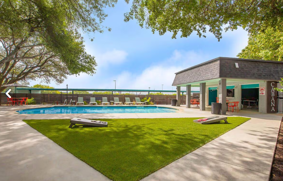 Backyard pool with green lawn, lounge chairs, and a covered patio under leafy trees