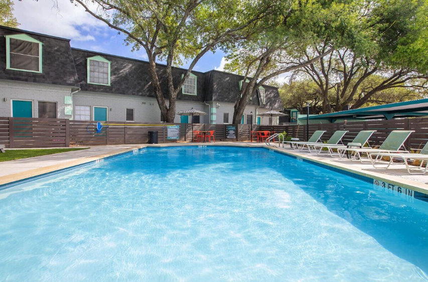 Outdoor apartment pool with lounge chairs and trees beside a building