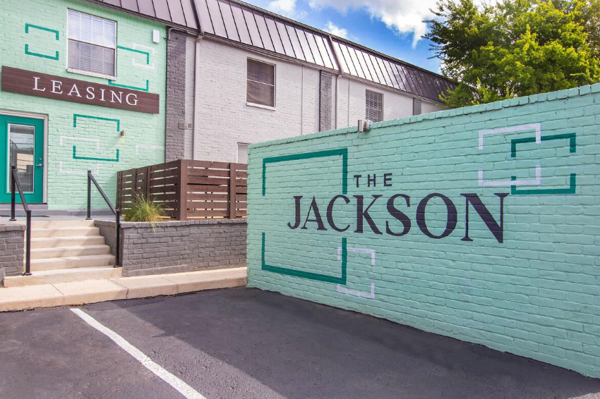 Leasing office exterior with turquoise wall sign reading “The Jackson” and a stairway entrance