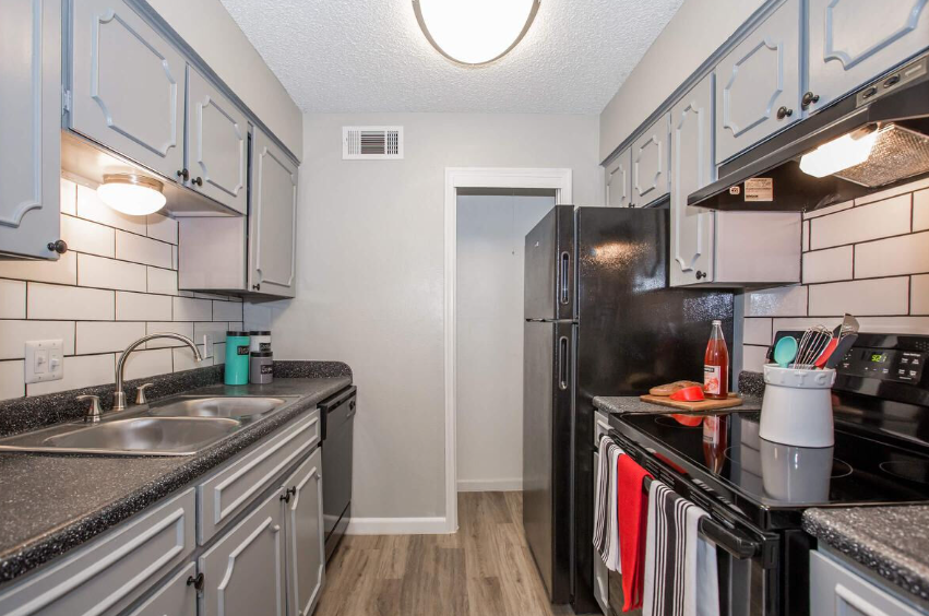 Narrow galley kitchen with gray cabinets, black appliances, and a white subway tile backsplash