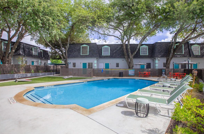 Courtyard apartment pool with lounge chairs, trees, and blue water under a cloudy sky