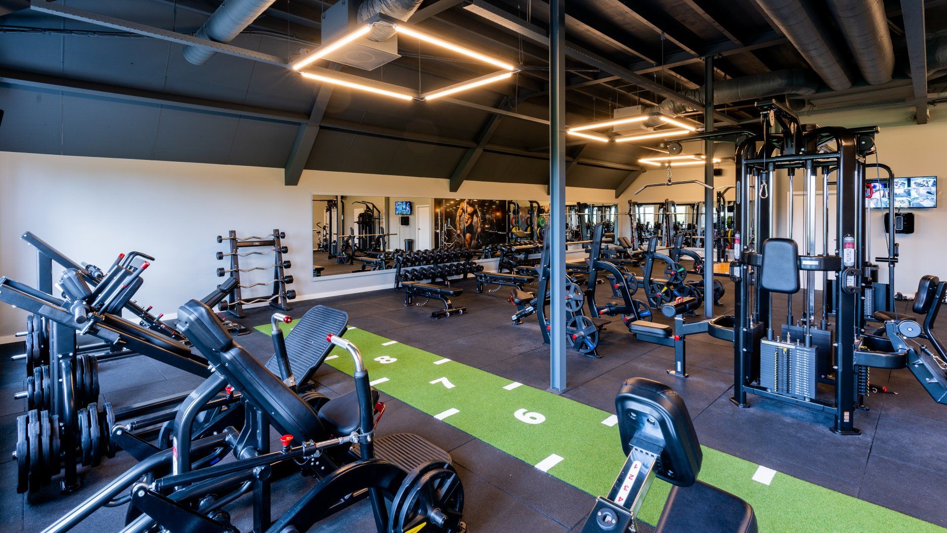 Sportschoolinterieur met gewichten, spiegels en een groene grasbaan.